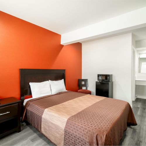 A modern hotel room with a double bed, side table, telephone, small fridge, and a mirror in the wash area at the far end of the room.