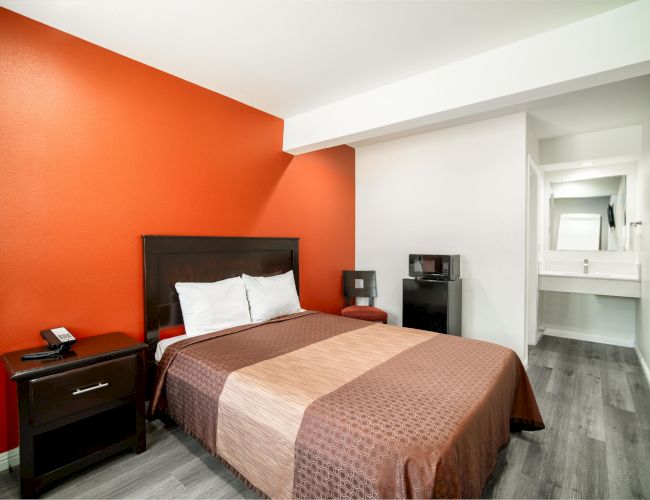 A modern hotel room with a double bed, side table, telephone, small fridge, and a mirror in the wash area at the far end of the room.