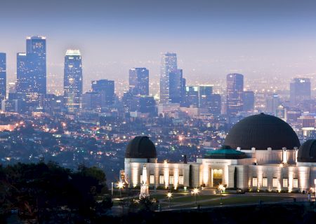 A large observatory sits prominently in the foreground, with a skyline of tall buildings and city lights twinkling in the background.