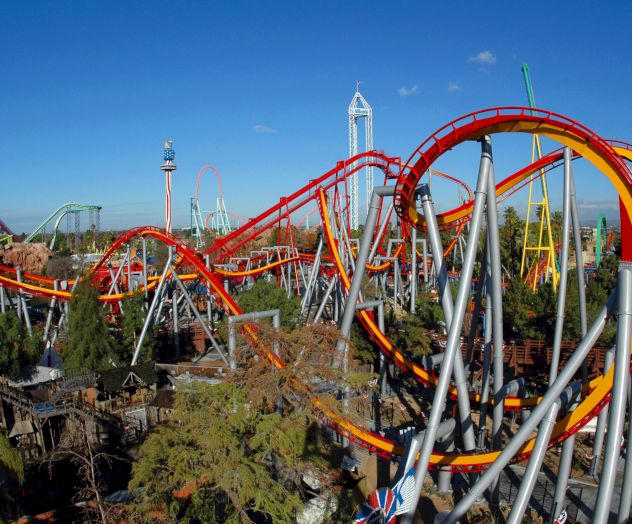 A vibrant amusement park with various roller coasters and attractions, featuring a prominent red and yellow track spiraling against a clear blue sky.