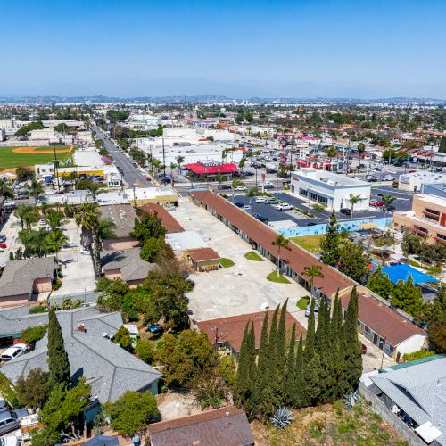 This aerial view shows a suburban neighborhood with houses, commercial buildings, and a sports field, all under a clear blue sky.