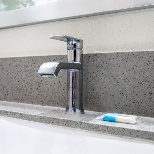 A modern bathroom sink with a chrome faucet, a bar of soap, and a mirror above it on a stone countertop.