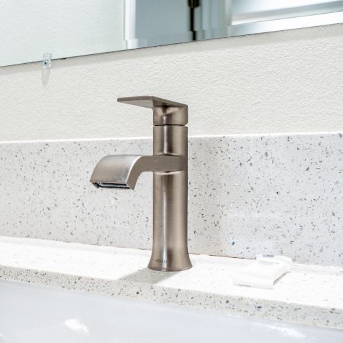 A modern bathroom sink with a sleek, brushed nickel faucet, set against a quartz countertop and a mounted mirror in the background.