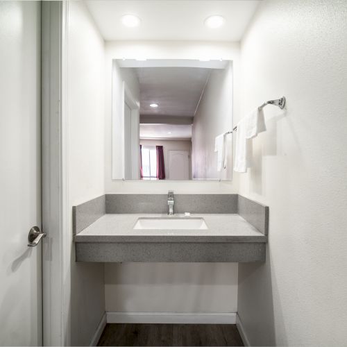 A minimalist bathroom with a modern sink, a large mirror, recessed lighting, white walls, and a towel rack with white towels.