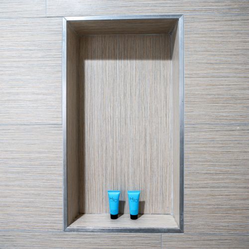 The image shows a wall niche in a tiled shower with two small blue bottles placed inside it.