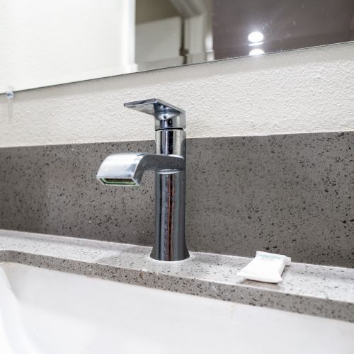 A modern bathroom sink with a chrome faucet, a small bar of soap on the countertop, and a mirror above the sink.