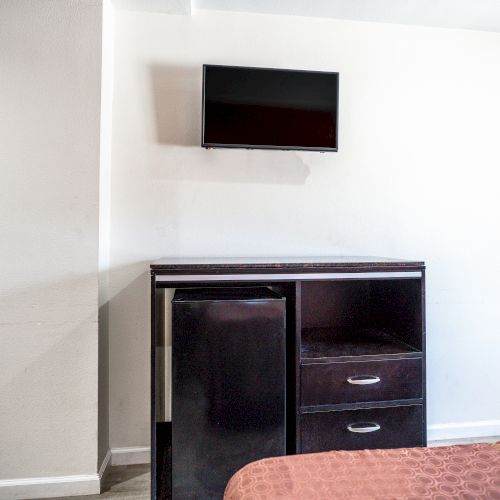 The image shows a hotel or bedroom corner with a small refrigerator and a flat-screen television mounted above it.